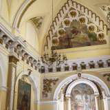...e infine nella chiesa. Ci troviamo in un ambiente riccamente ornato e coperto da volte a botte color ocra, con lunette con floreali bianche e brune, da cui scendono piccoli lampadari di cristallo